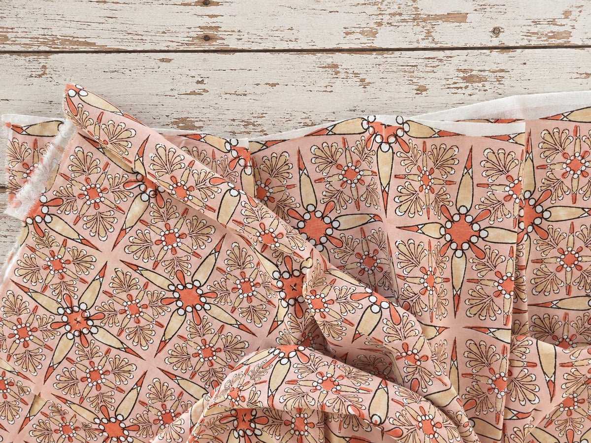 Soft peach cotton fabric with repeating floral starburst pattern shown in a drape