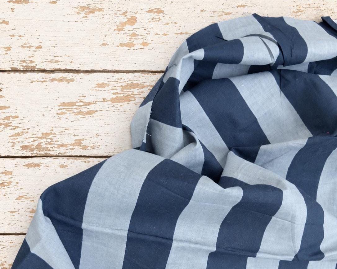 Navy and light blue striped fabric draped across a rustic wooden background, showing its folds and pattern.