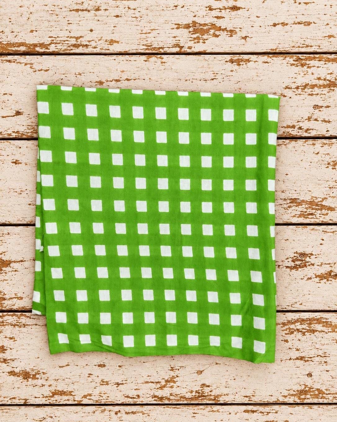 Vivid green gingham fabric with evenly spaced white checks folded on a rustic wooden surface.