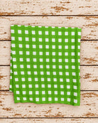 Vivid green gingham fabric with evenly spaced white checks folded on a rustic wooden surface.