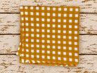 Folded golden mustard and white checked fabric displayed on distressed wooden boards.
