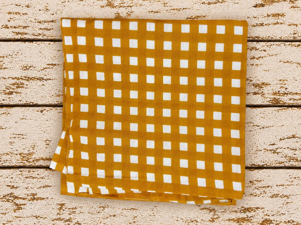 Folded golden mustard and white checked fabric displayed on distressed wooden boards.