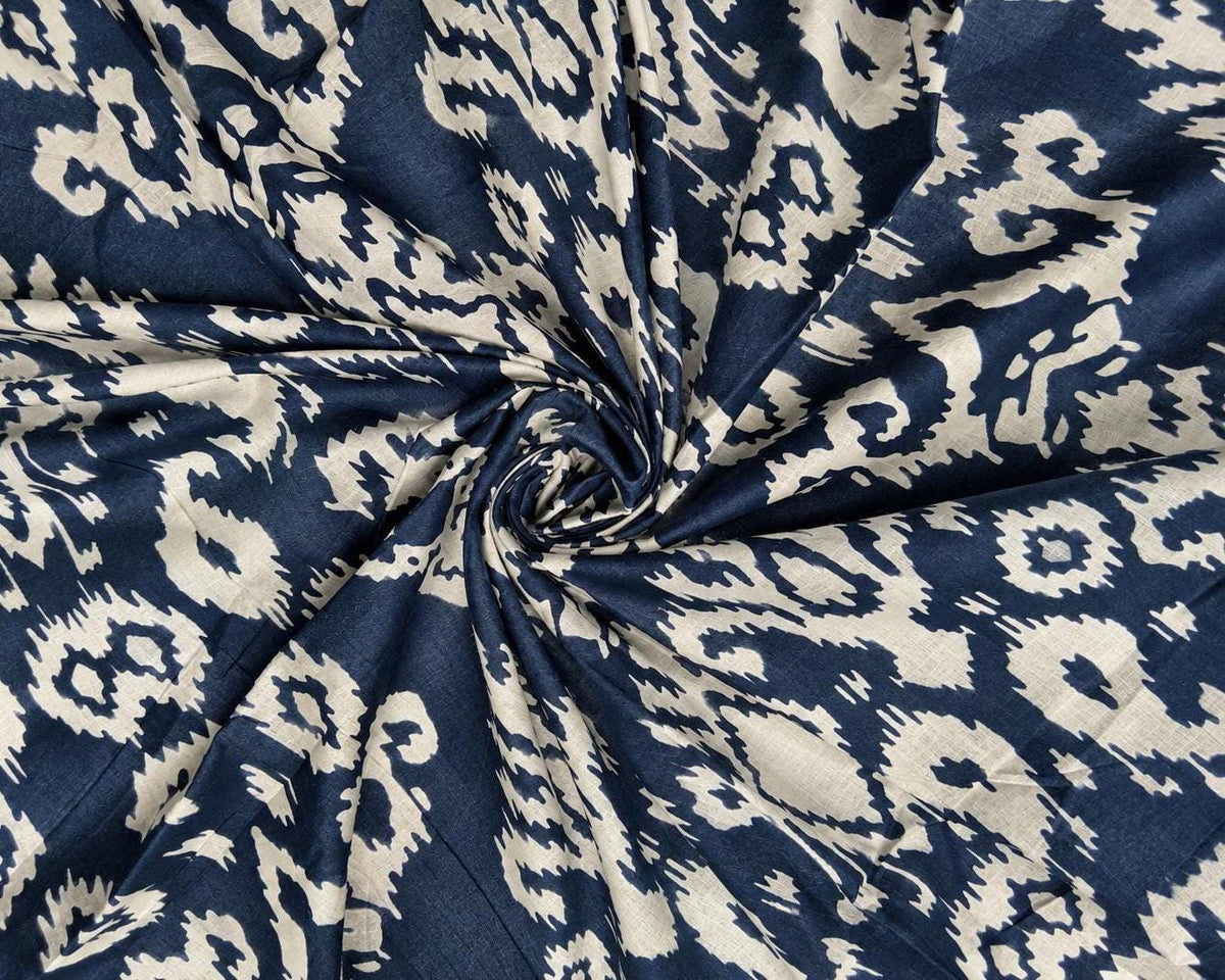 Close-up of navy and cream printed cotton fabric showing its irregular ornamental ikat-style pattern and woven texture.