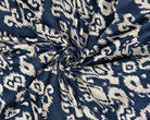 Close-up of navy and cream printed cotton fabric showing its irregular ornamental ikat-style pattern and woven texture.