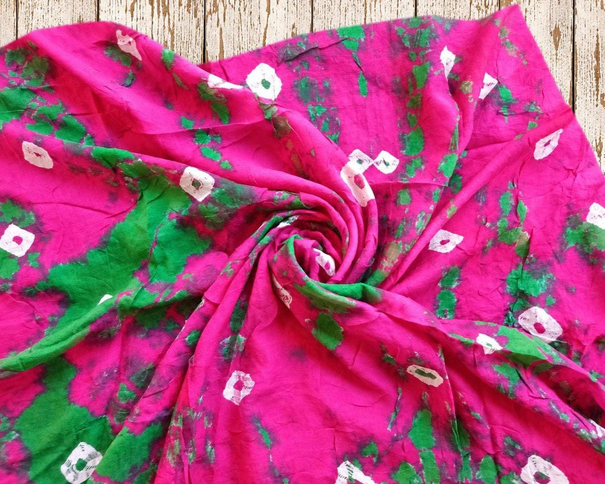 Close-up of soft pink and green vintage sari fabric arranged in a spiral to show its flowing texture and irregular tie-dye pattern.