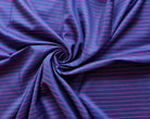 Close-up of soft blue-purple sari fabric arranged in folds, showing fine magenta stripes and the sheen of the textile.