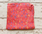 Close view of coral-red fabric with scattered blue flowers, yellow blossoms and green decorative motifs.