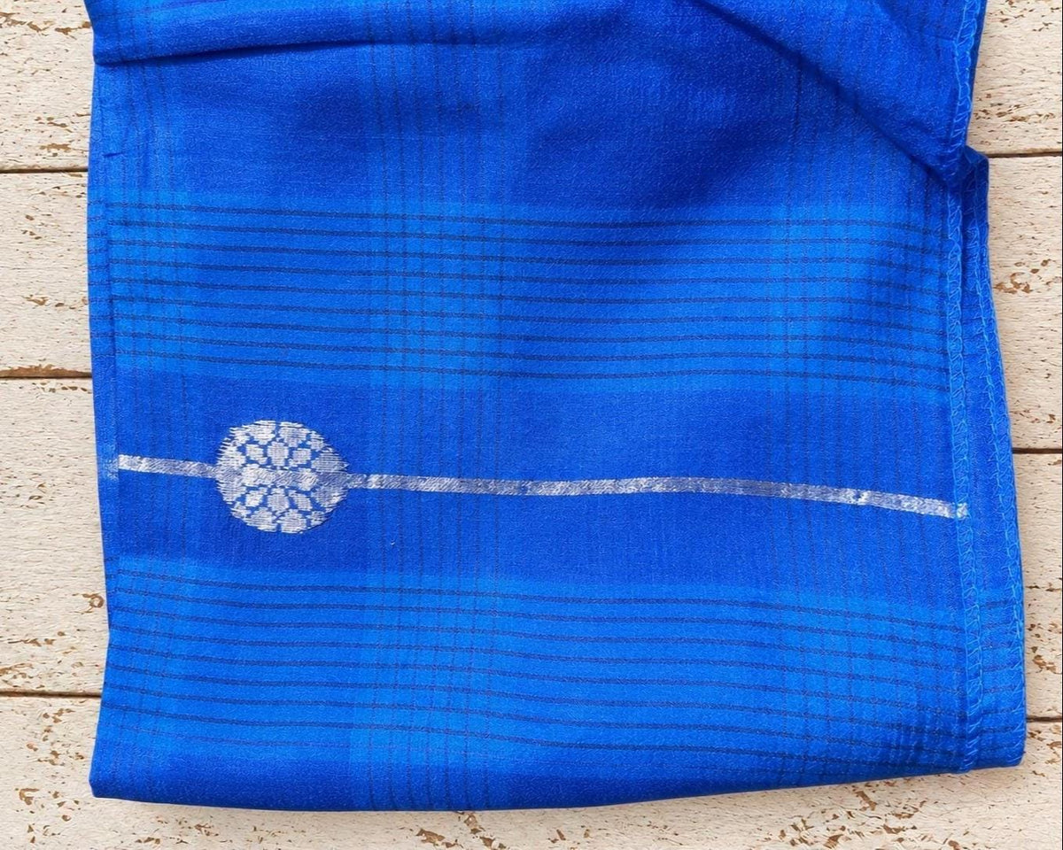 Close-up of a silver decorative motif on blue checked woven fabric with stitched edging.
