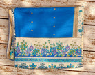 Folded vintage pure silk sari fabric showing its blue body, floral border and decorative edging.