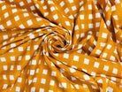 Close-up of golden mustard fabric showing its repeating white check pattern and texture.