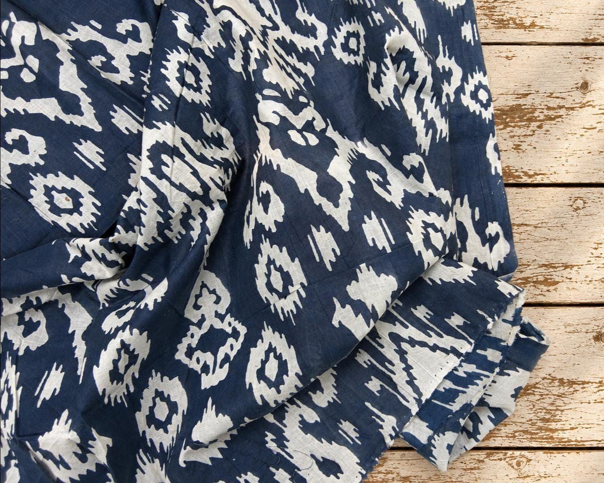 Navy blue cotton fabric with irregular cream ikat-inspired motifs draped over a rustic wooden surface.