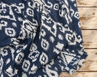Navy blue cotton fabric with irregular cream ikat-inspired motifs draped over a rustic wooden surface.