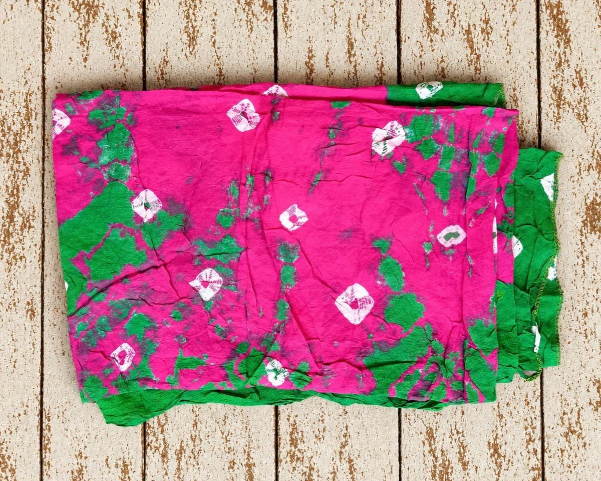 Vintage sari fabric in bright pink and green with scattered white motifs, folded to show the tie-dye pattern.
