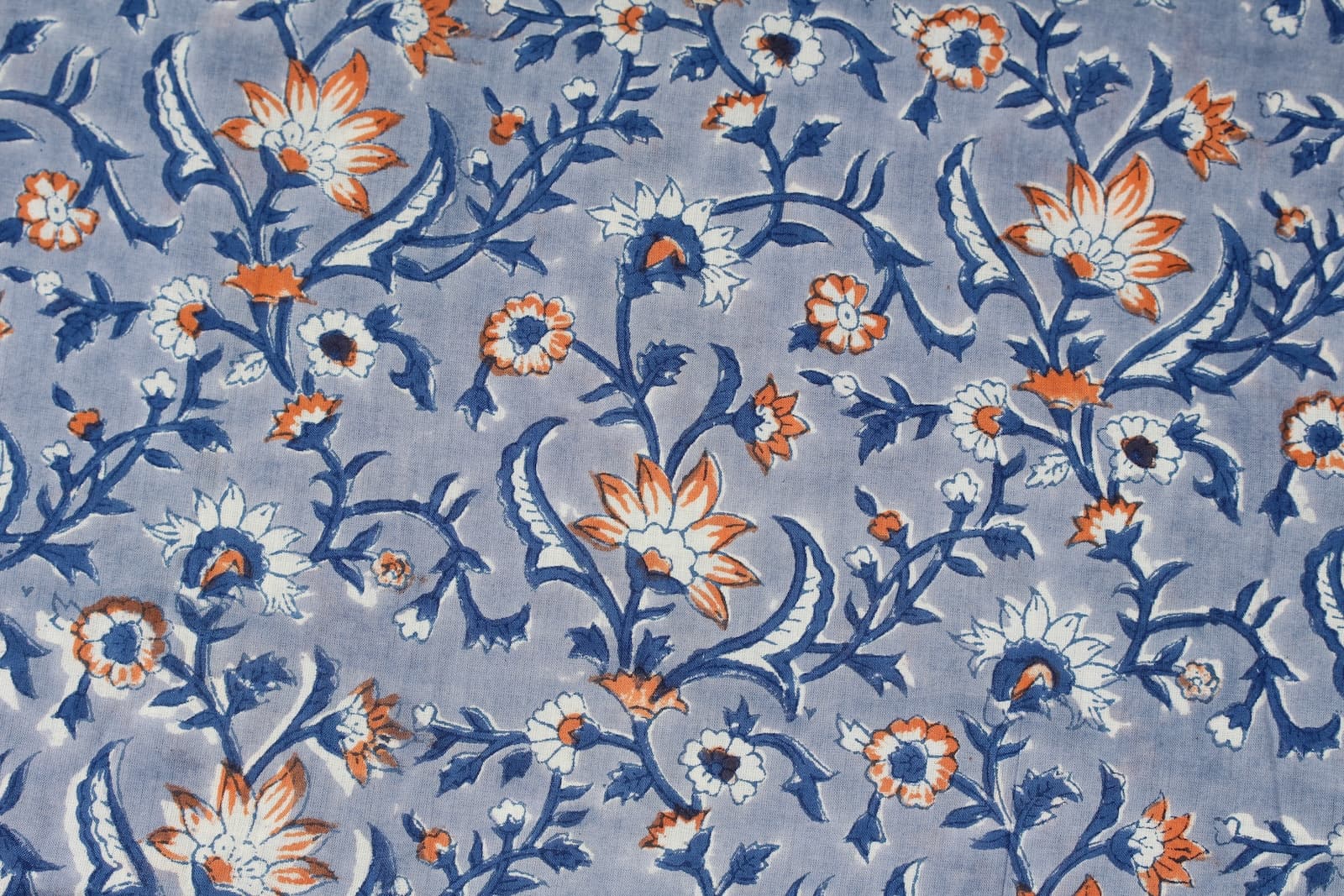 Close-up of ivory and orange floral motifs with indigo botanical vines on hand printed cotton fabric