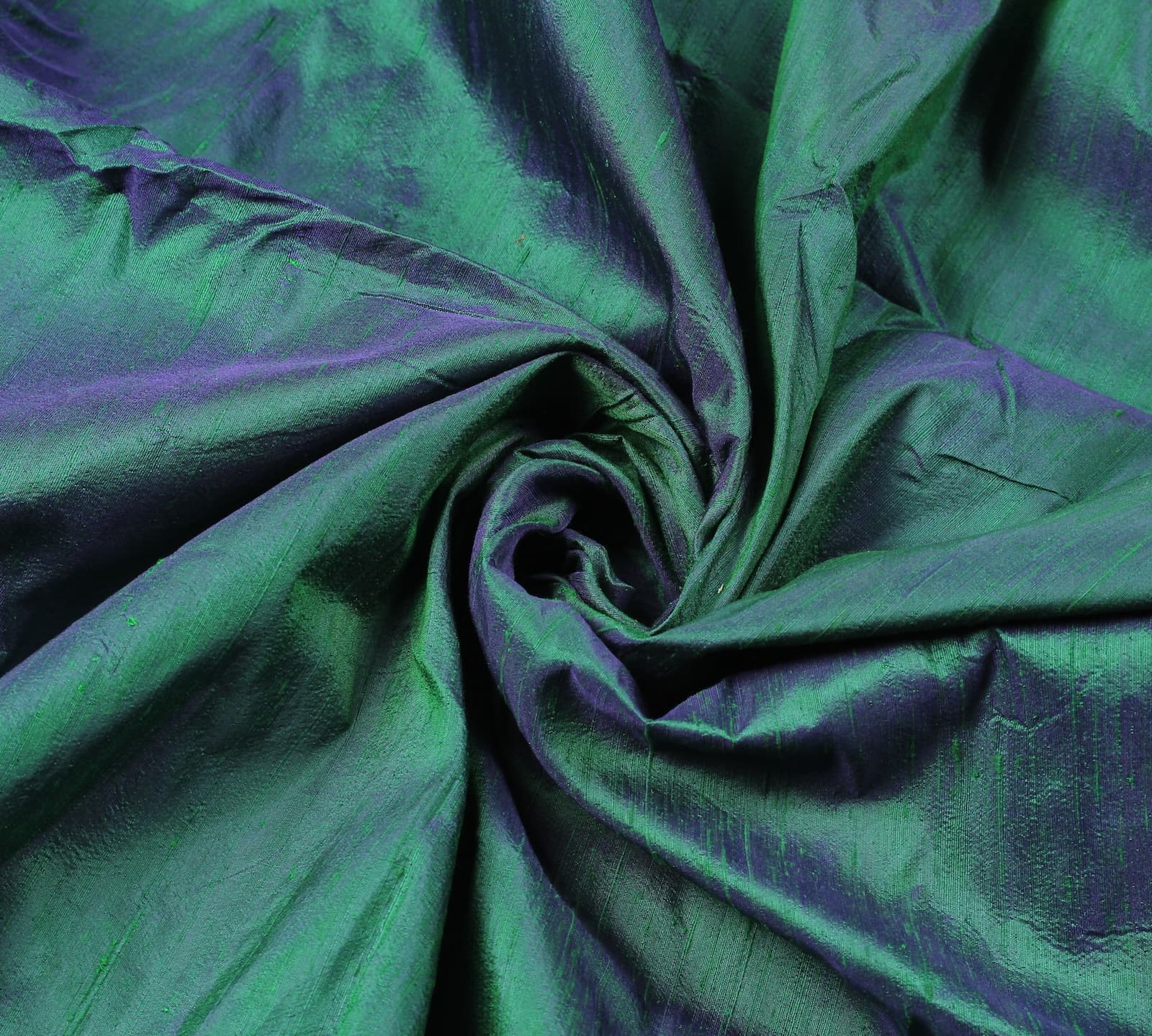 Peacock Lagoon dupion silk fabric arranged in a swirl highlighting peacock blue and emerald green colour shifts with natural silk texture