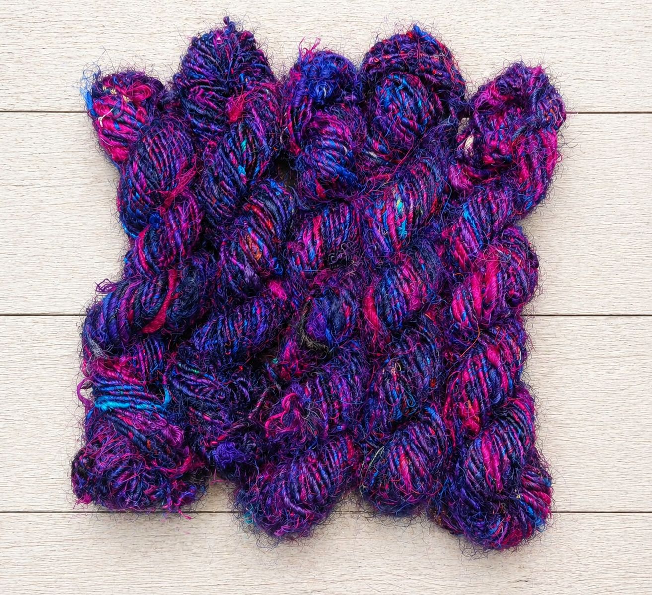 Multiple skeins of Jewel Tones recycled sari silk yarn featuring rich purple, pink and blue fibres.