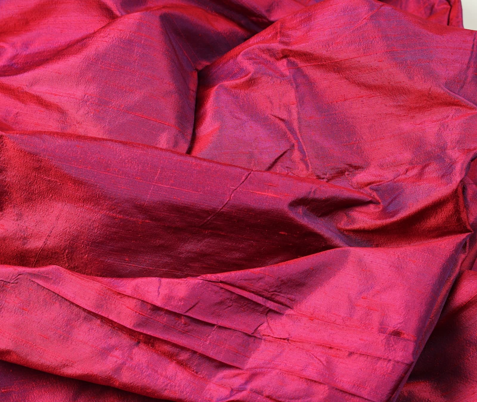 Magenta Orchid dupion silk fabric folded on a rustic tabletop showing iridescent magenta silk yardage and natural slub texture