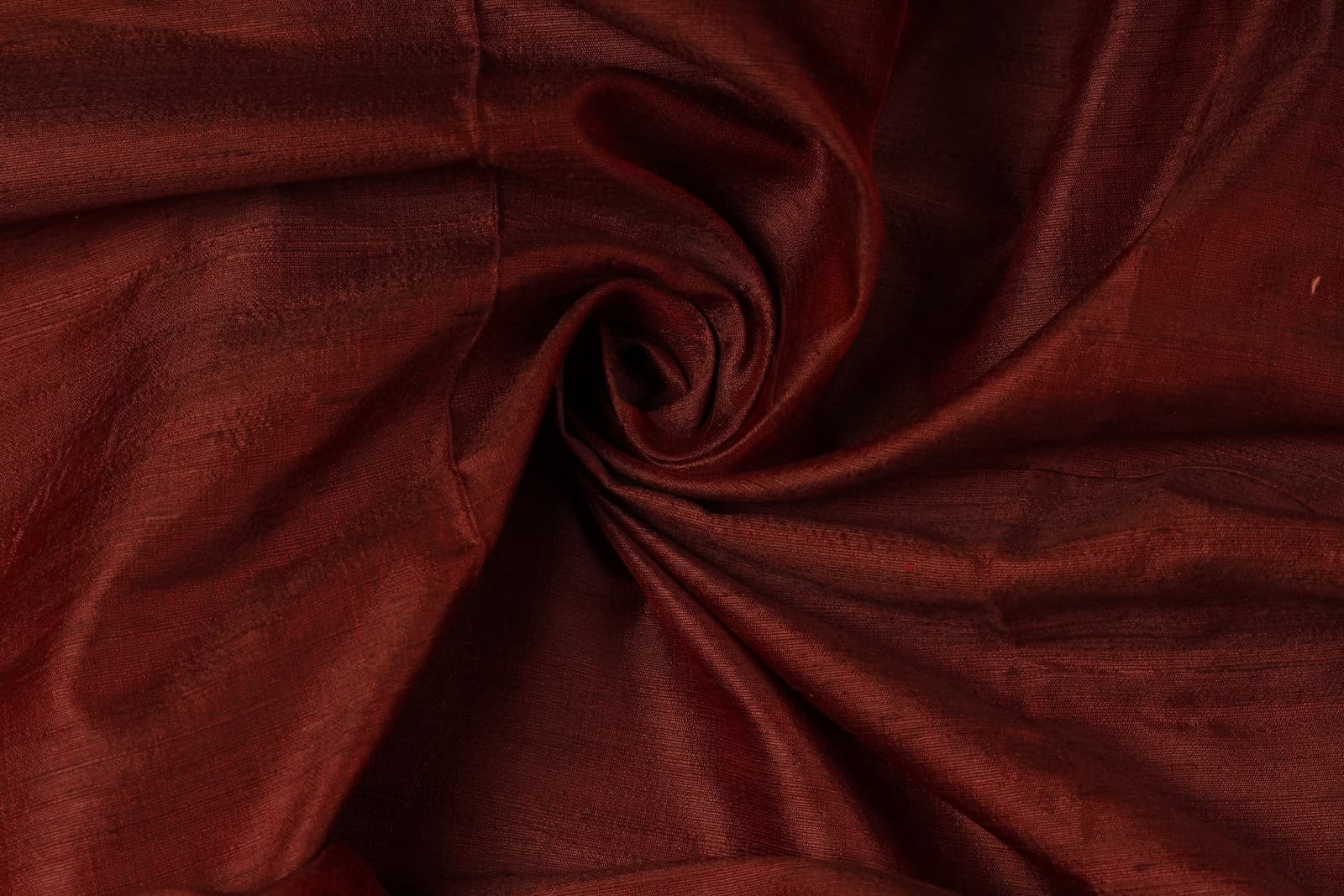 Mahogany Burgundy Dupion Silk Fabric arranged in elegant swirling folds highlighting its lustrous finish and natural dupion silk texture
