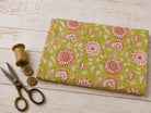 Olive Blossom block printed cotton fabric folded on a white wooden surface with vintage scissors and thread spool