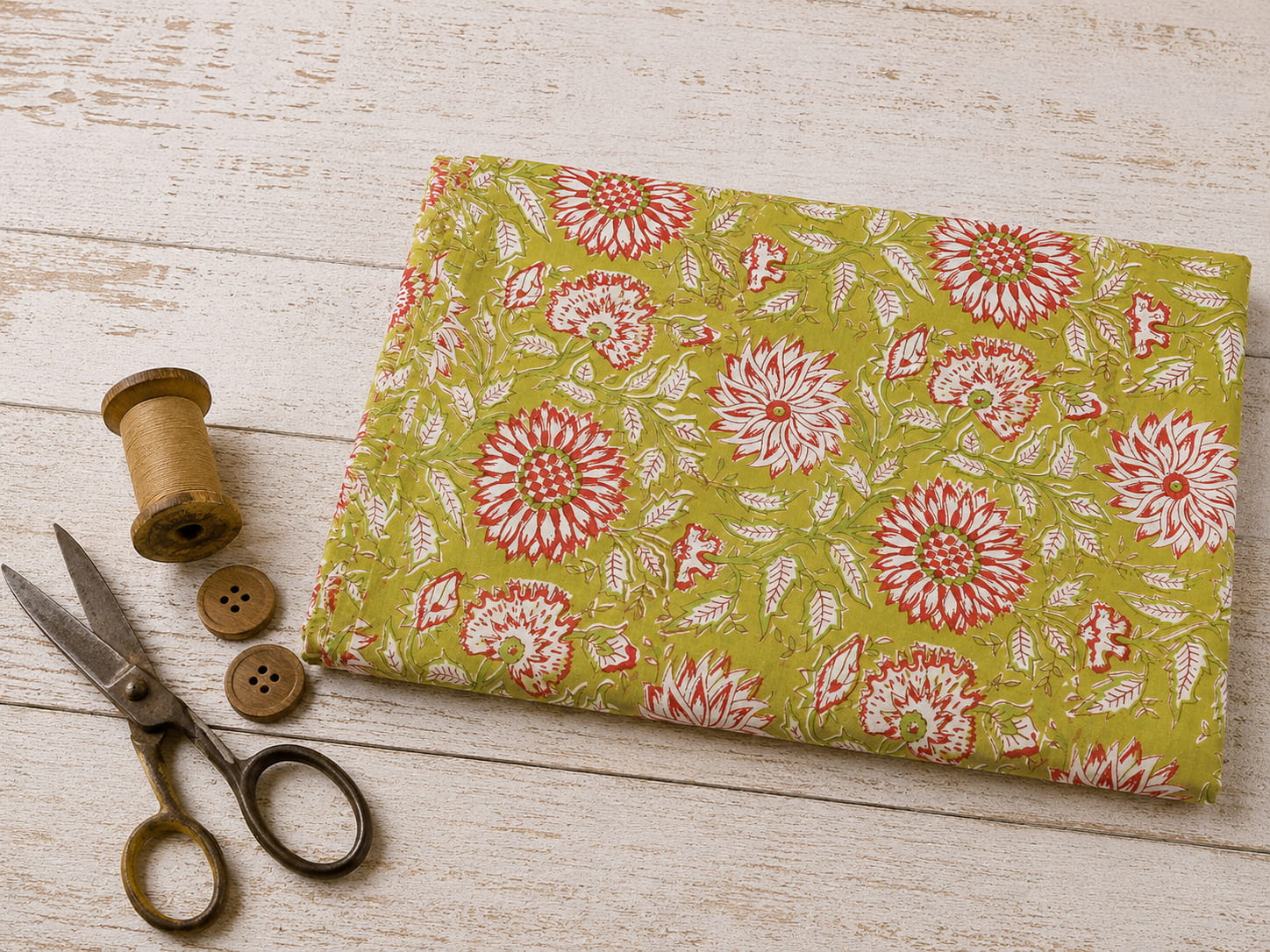 Olive Blossom block printed cotton fabric folded on a white wooden surface with vintage scissors and thread spool