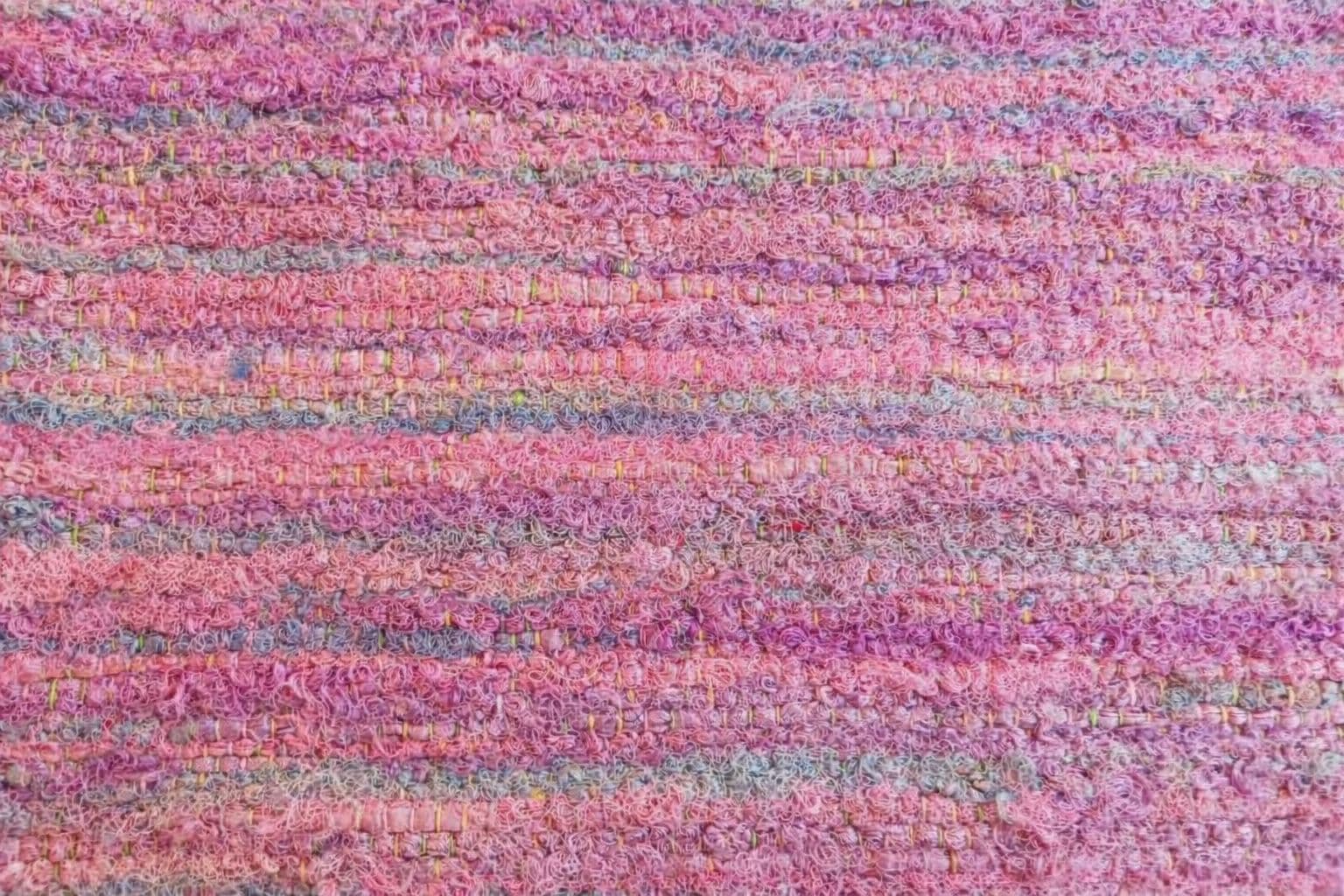 Close-up of handwoven sari ribbon fabric showing textured pastel pink, lilac, and pale blue silk ribbons.