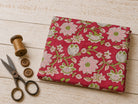 Raspberry Lotus Vine block printed cotton fabric folded on a wooden surface with vintage sewing scissors and wooden thread spool
