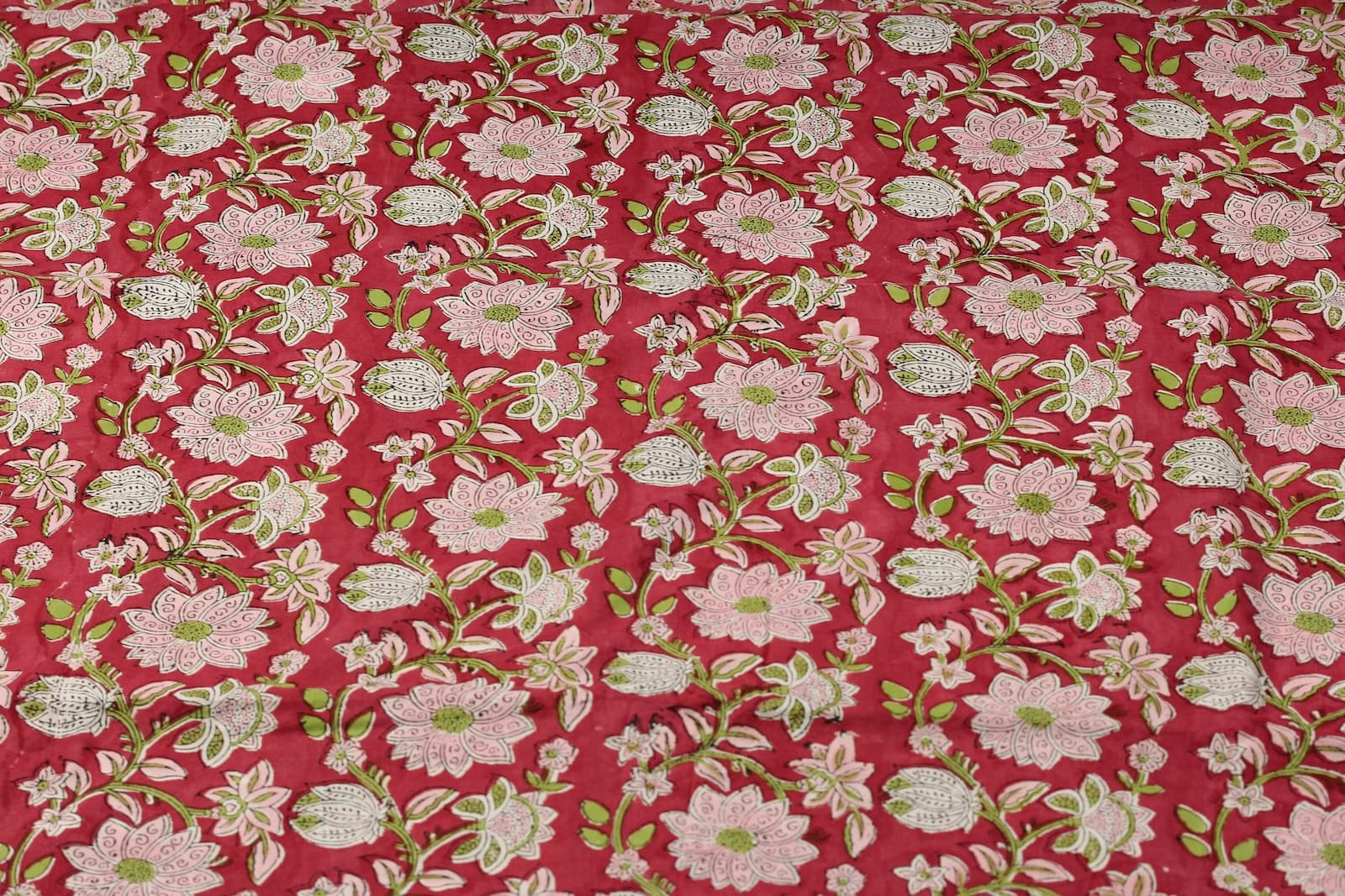 Raspberry Lotus Vine hand block printed cotton fabric featuring pink lotus flowers and green vines on a raspberry red background