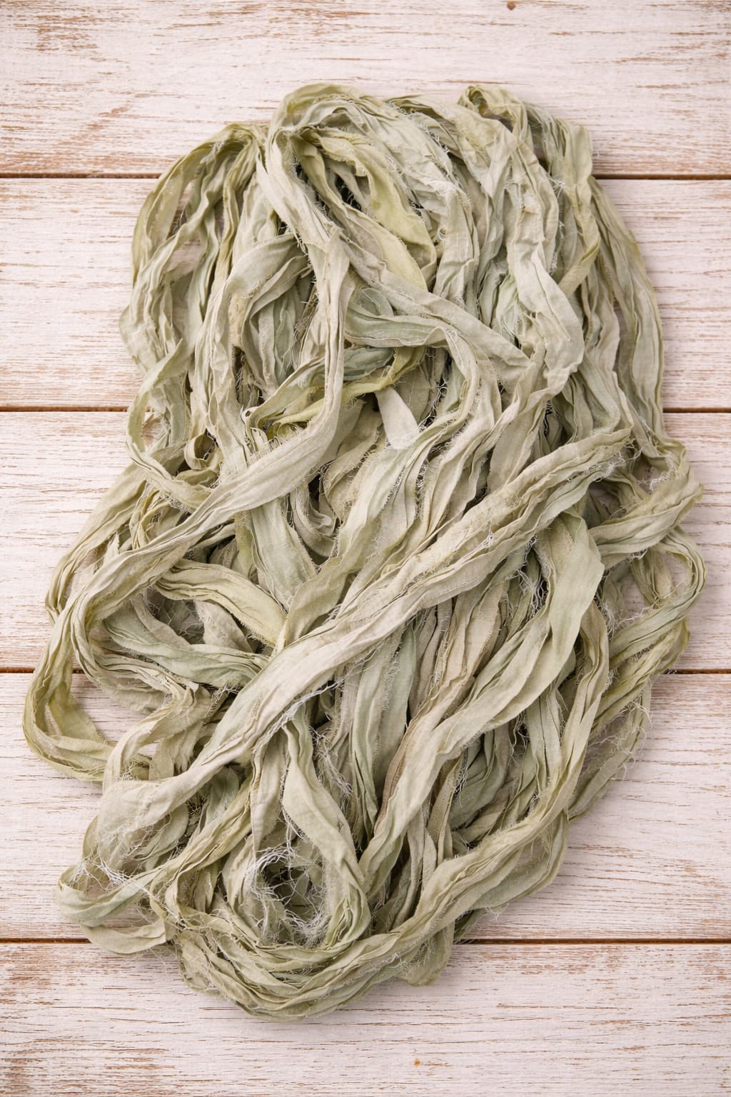 Loose pile of Faded Sage sari silk ribbon featuring soft sage green and pale eucalyptus tones.