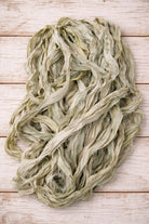Loose pile of Faded Sage sari silk ribbon featuring soft sage green and pale eucalyptus tones.