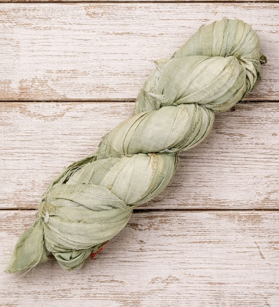 Single skein of sage green sari silk ribbon handcrafted from recycled silk fabric.