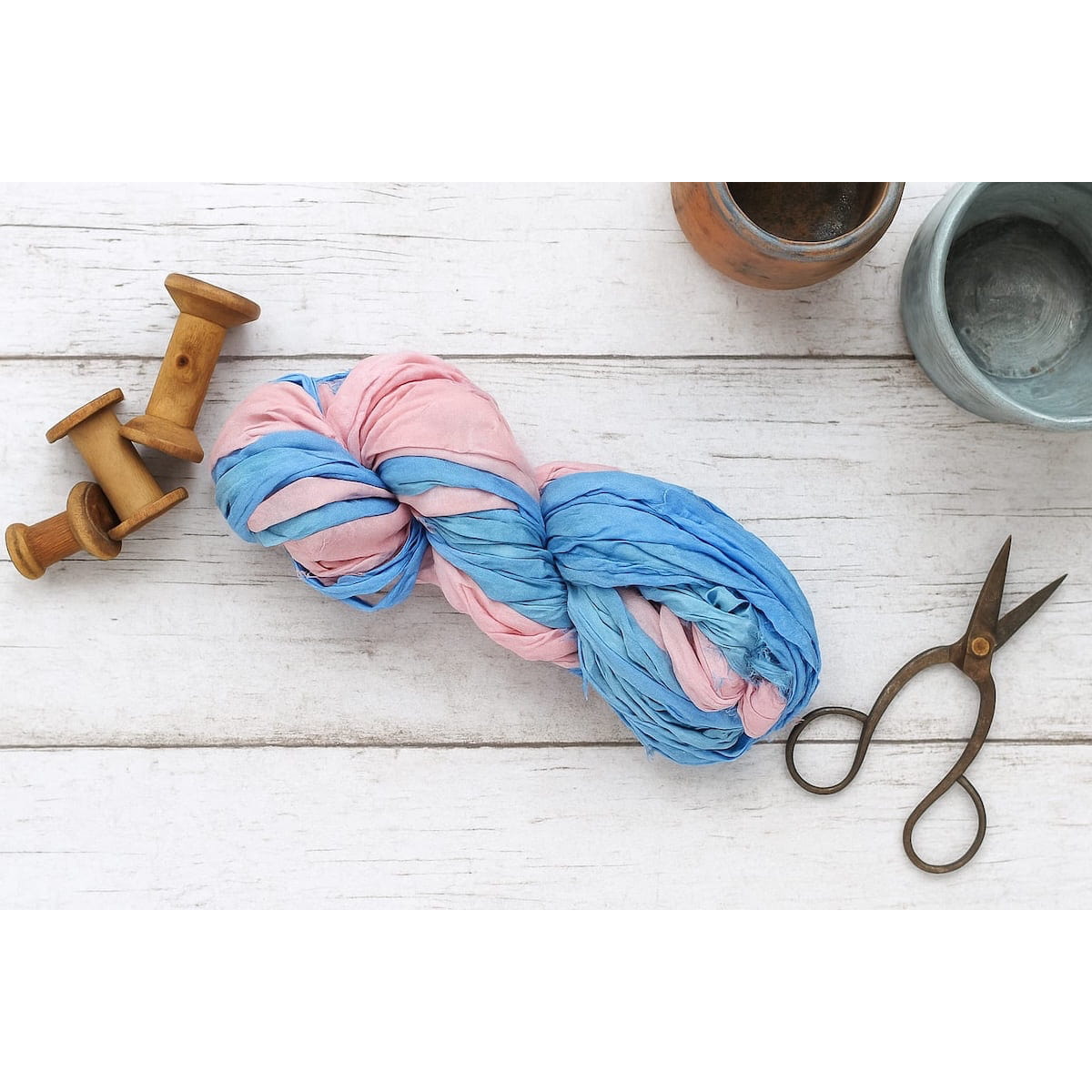 Flat lay of pastel pink and sky blue sari silk ribbon on a neutral backdrop with props, showcasing its versatility for crafts and handmade projects.