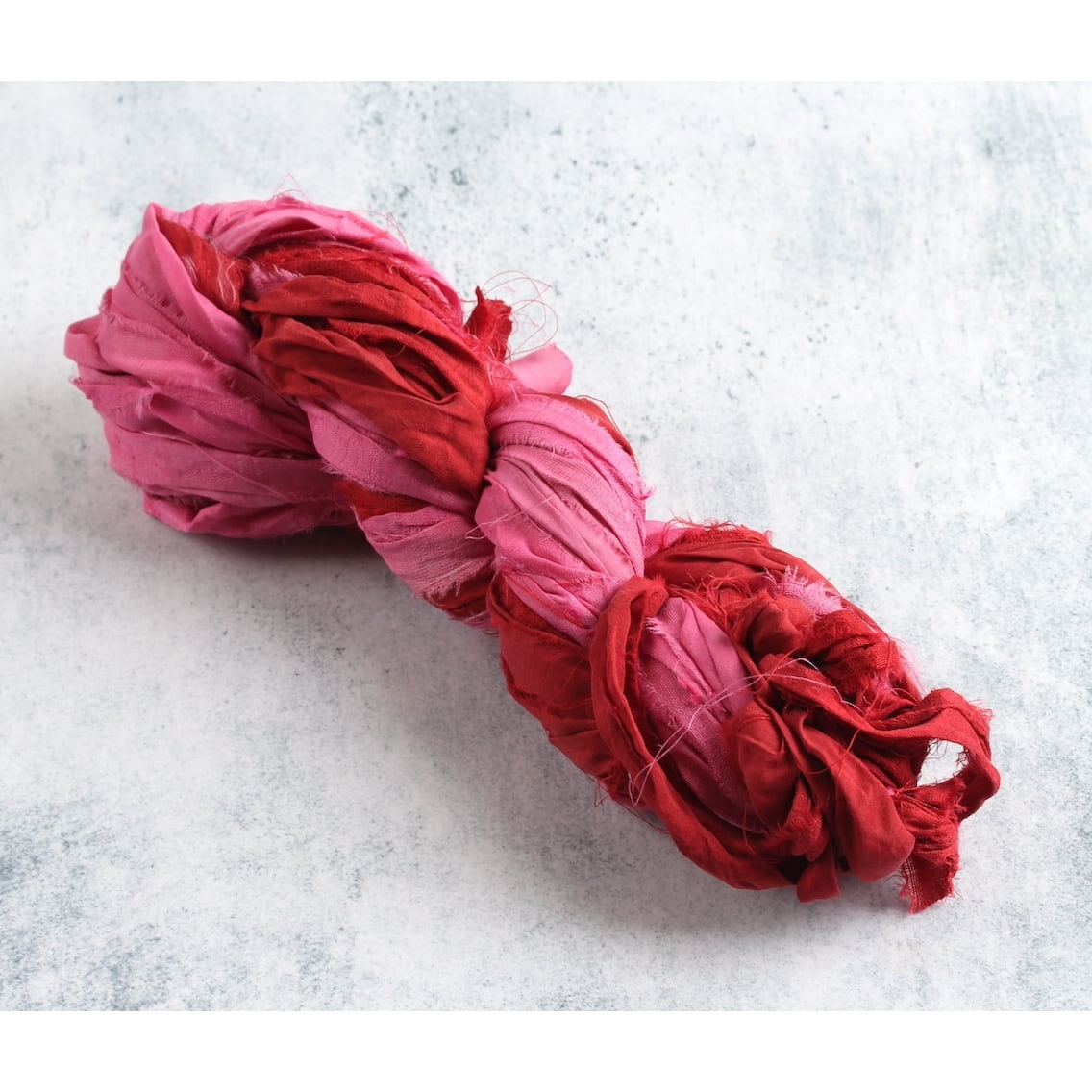 Red and pink sari silk ribbon skein on white background, handmade from recycled sari silk, eco-friendly craft supply.