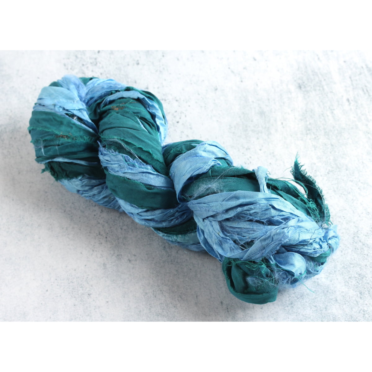 Sky blue and teal sari silk ribbon skein on white background, handmade from recycled sari silk, perfect for crafts and DIY.