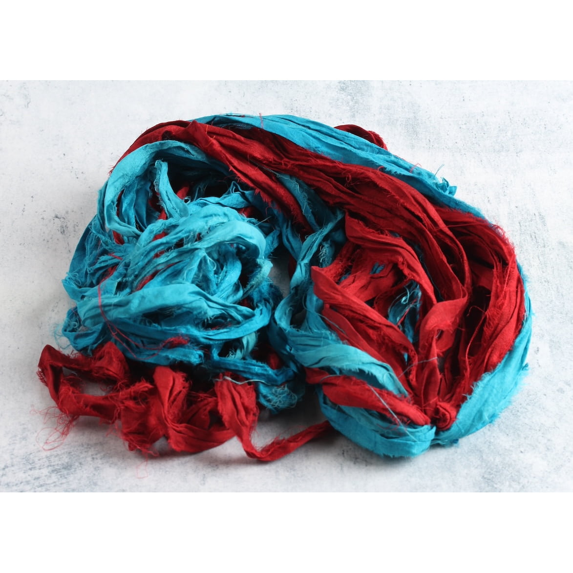 Open view of turquoise and red sari silk ribbon showing hand-dyed colors and frayed edges.