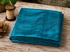 Turquoise Blue Dupion Silk Fabric folded on a rustic wooden table showing vibrant aqua-blue colour, natural slub texture, and lustrous silk sheen
