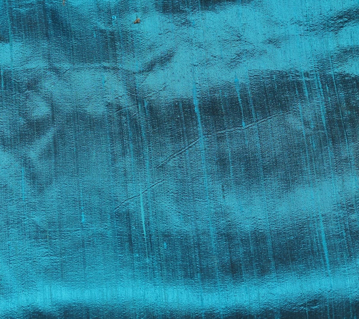 Close-up of Turquoise Blue Dupion Silk Fabric showing natural slub texture, woven silk character, and shimmering aqua-blue finish