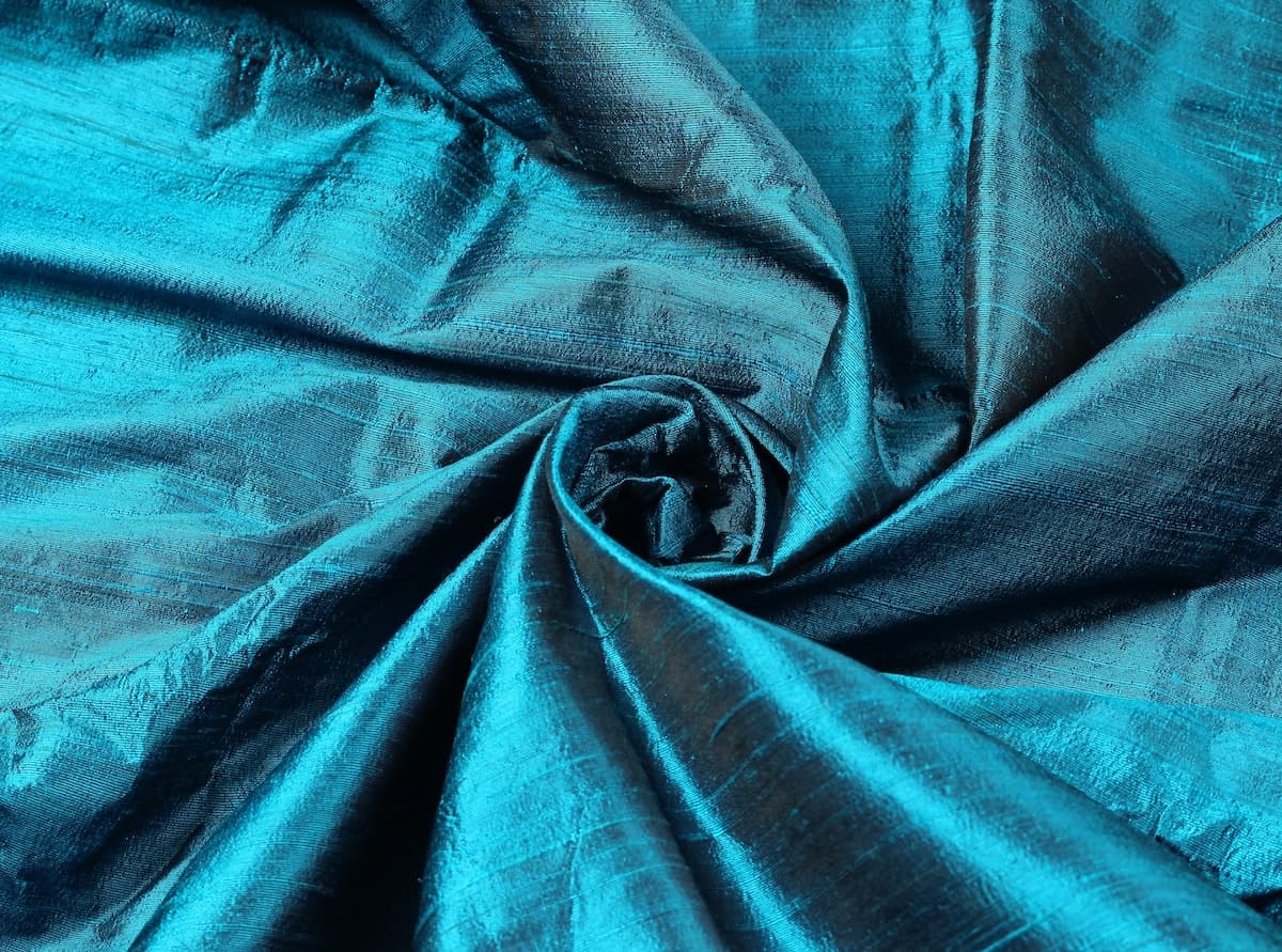 Turquoise Blue Dupion Silk Fabric arranged in elegant folds highlighting its iridescent sheen, crisp texture, and vibrant blue-green tones